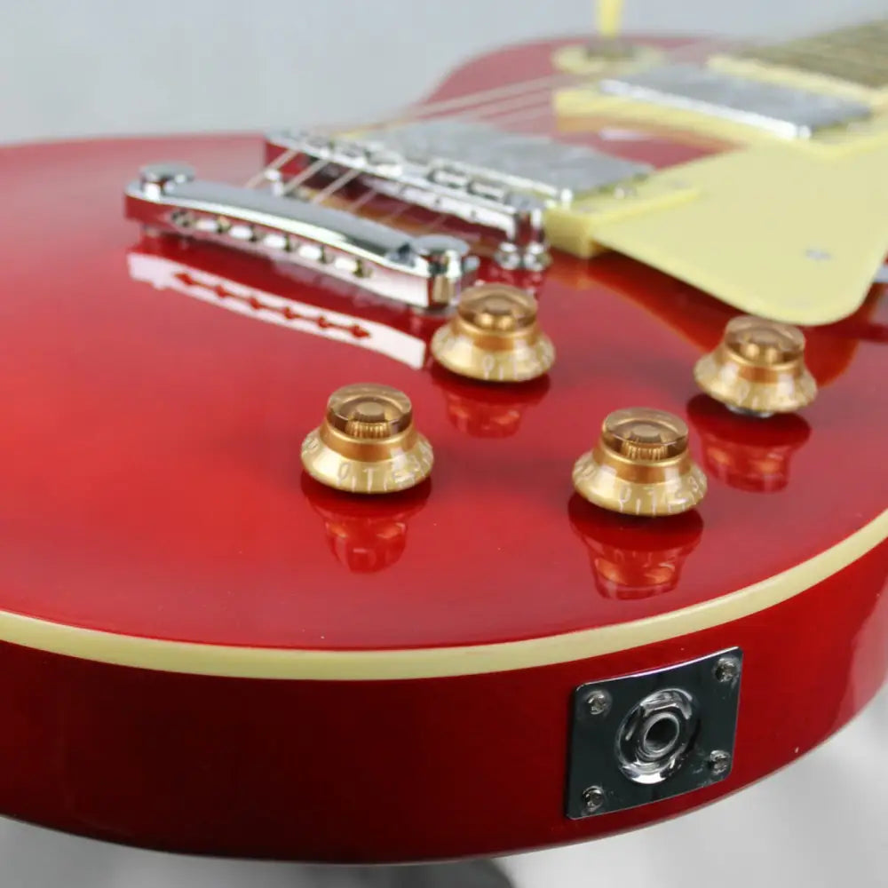 Close-up of the shiny red Axiom Challenger electric guitar body with gold control knobs