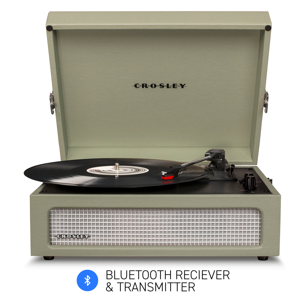 The Crosley Voyager Sage Bluetooth Portable Turntable by Crosley is shown with the lid open, playing a vinyl record. The front panel includes a speaker grille, control knobs, and RCA outputs for easy connectivity.