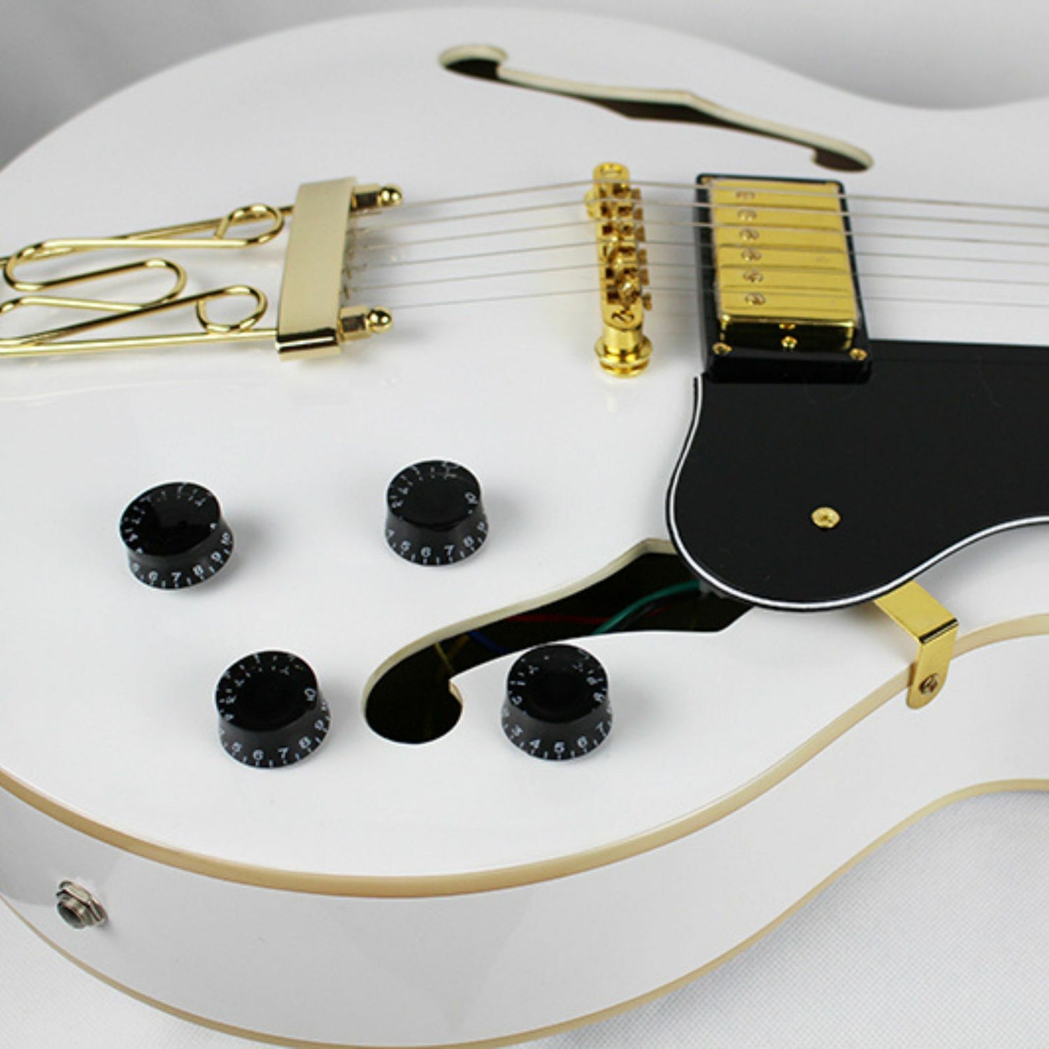 The Axiom Music Axiom Columbia Archtop Electric Guitar White Bird features a white hollow body, gold hardware, black pickguard, vintage-style humbuckers, four knobs, two pickups, and f-hole cutouts.
